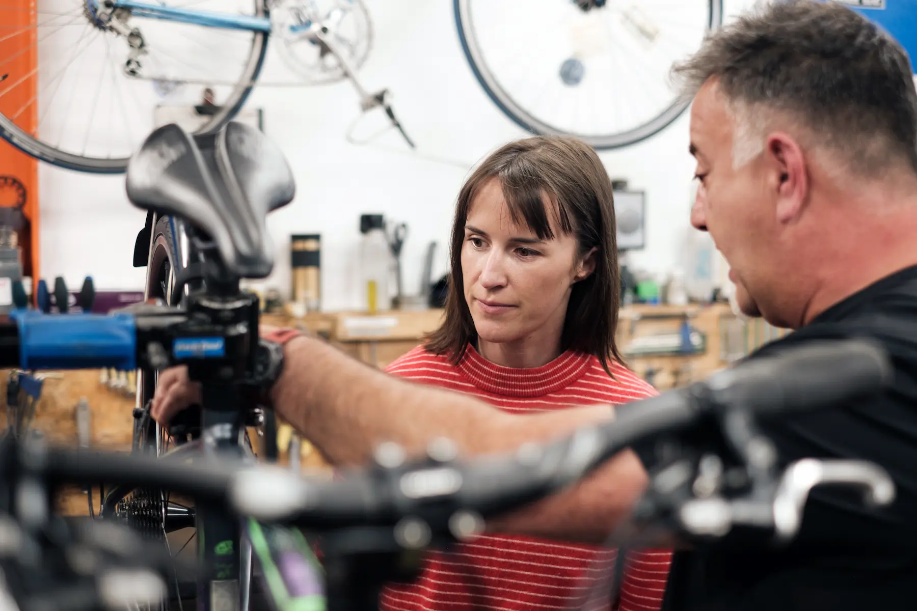 A bike mechanic on the right of the image shows a person in a red striped top the back of a wheel he is repaiting